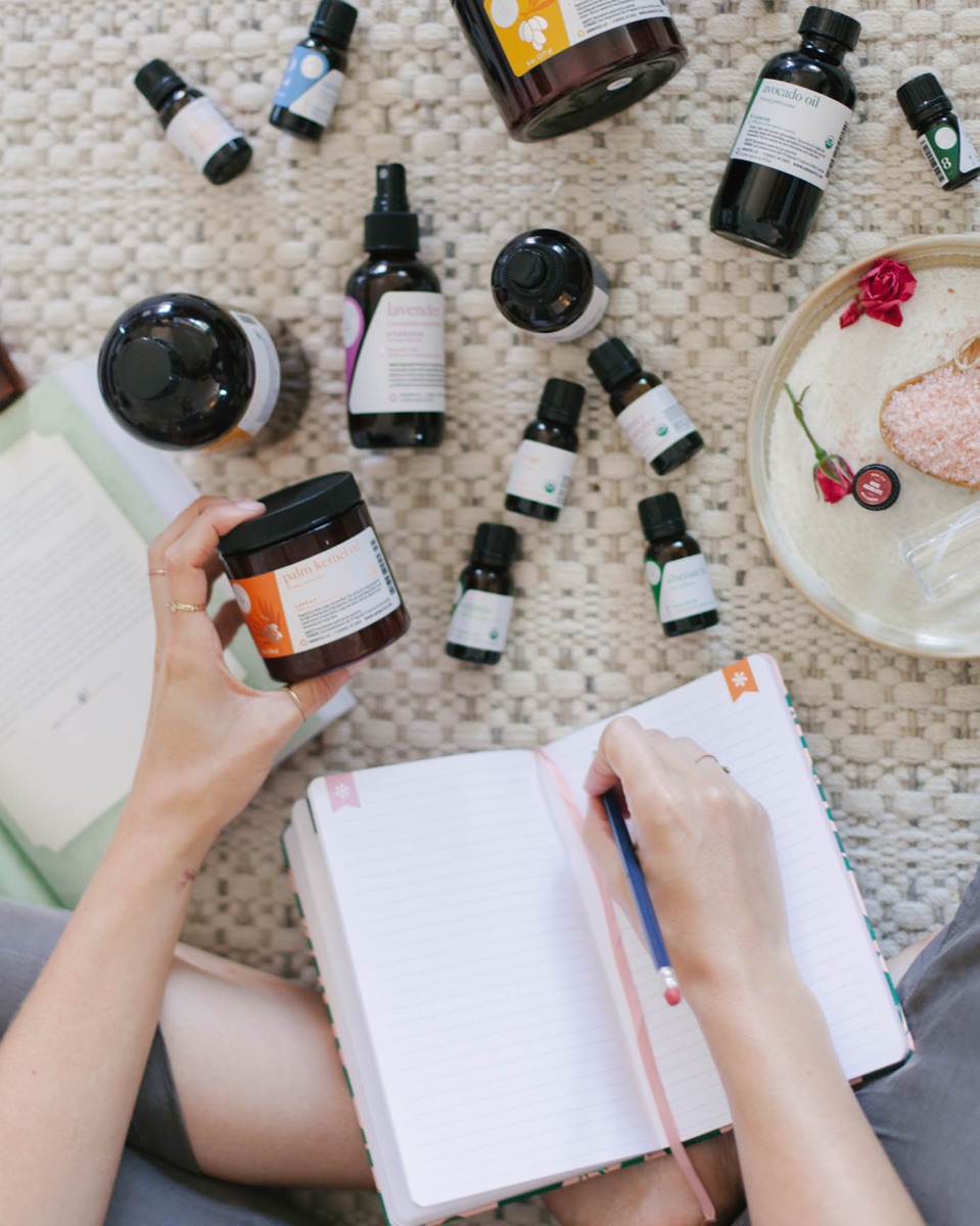 Hands choosing essential oils beside an open blending notebook